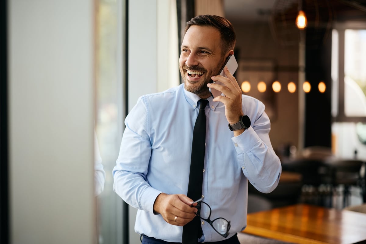 Happy businessman talking on cell phone by the window in a cafe. Copy space.